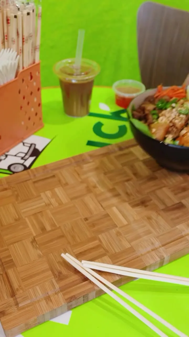 Our combination vermicelli bowl and an iced drink on the lime-green table, with a bamboo board and chopsticks