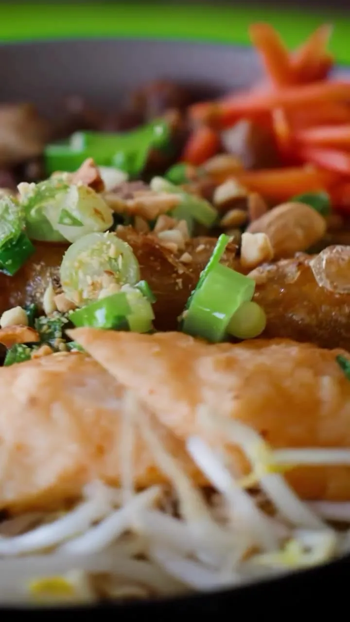 Close up of a vermicelli bowl: crisp spring roll, crushed peanuts, spring onion and pickled carrot over bean sprouts